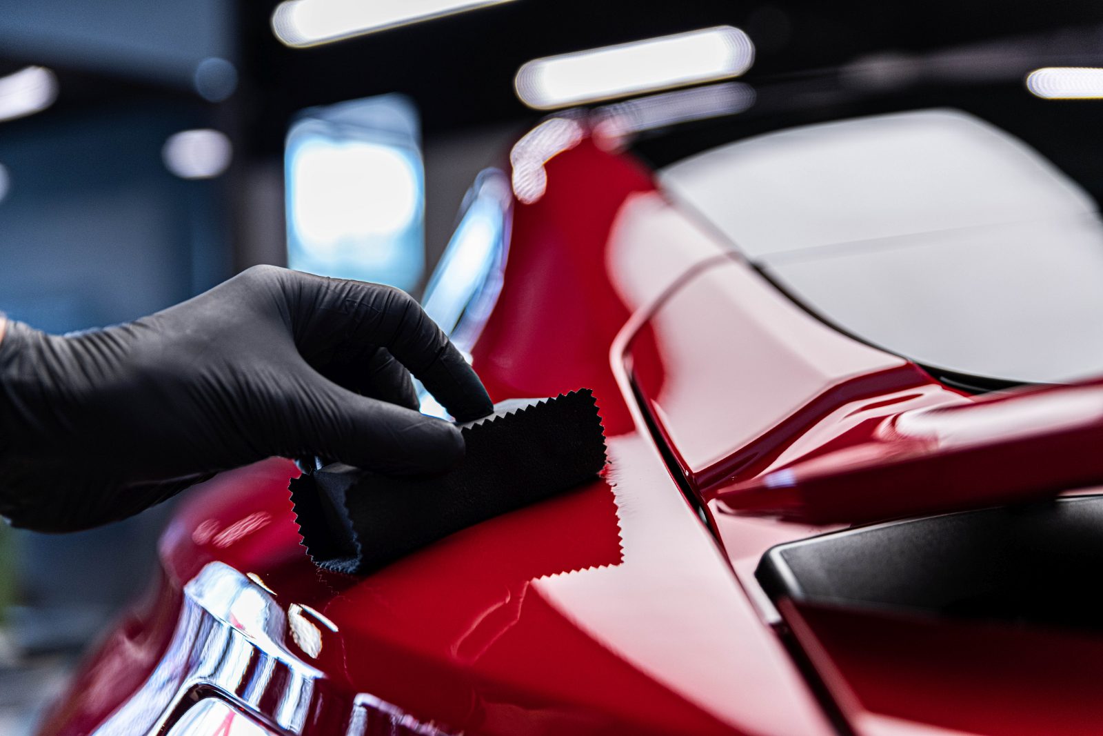 Hand in black glove polishing red car surface with microfiber cloth