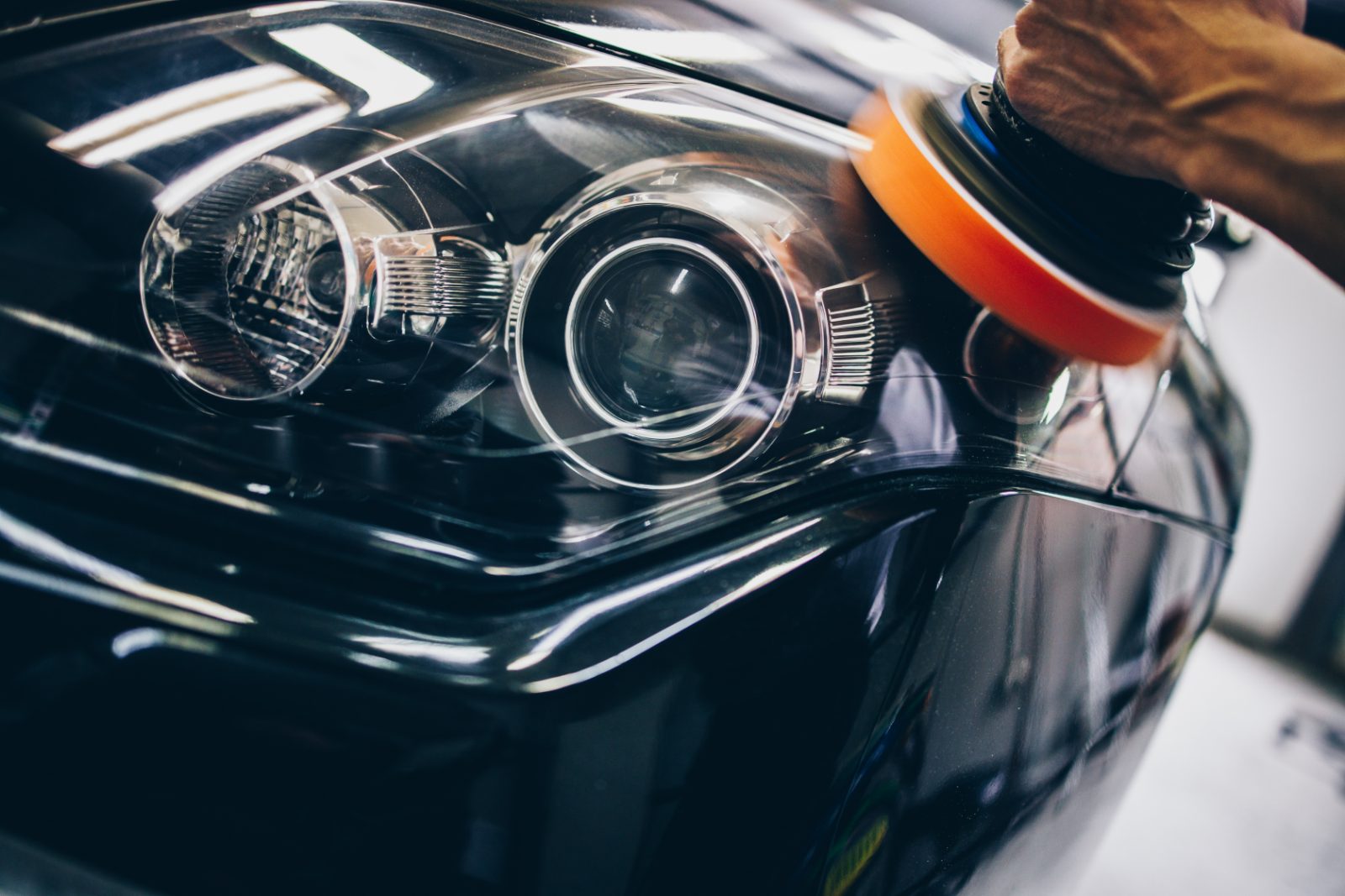 Close-up of black car headlight with LED ring light and person's hand in brown jacket