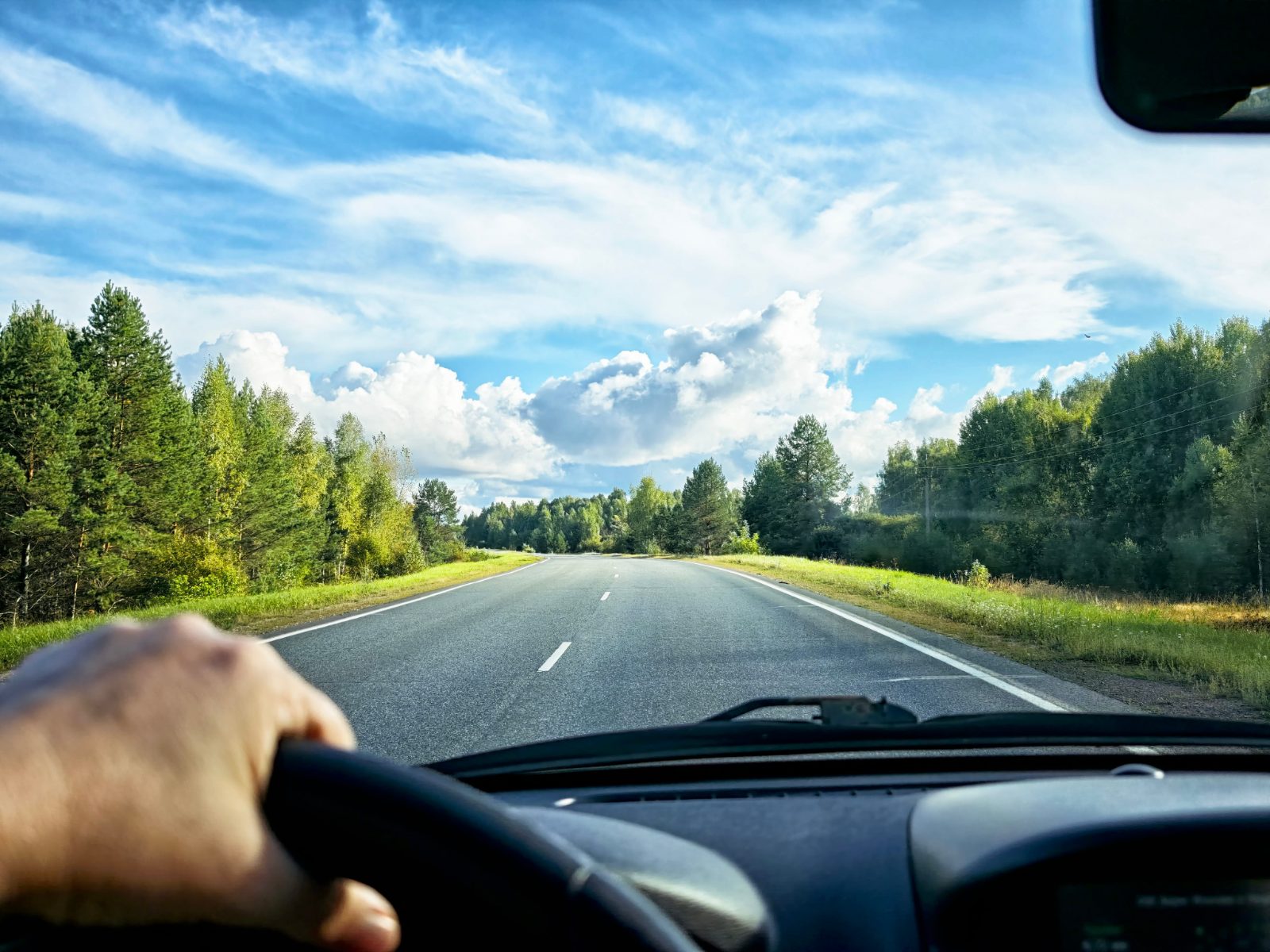 Driver's perspective on a straight forest road with blue sky and white clouds
