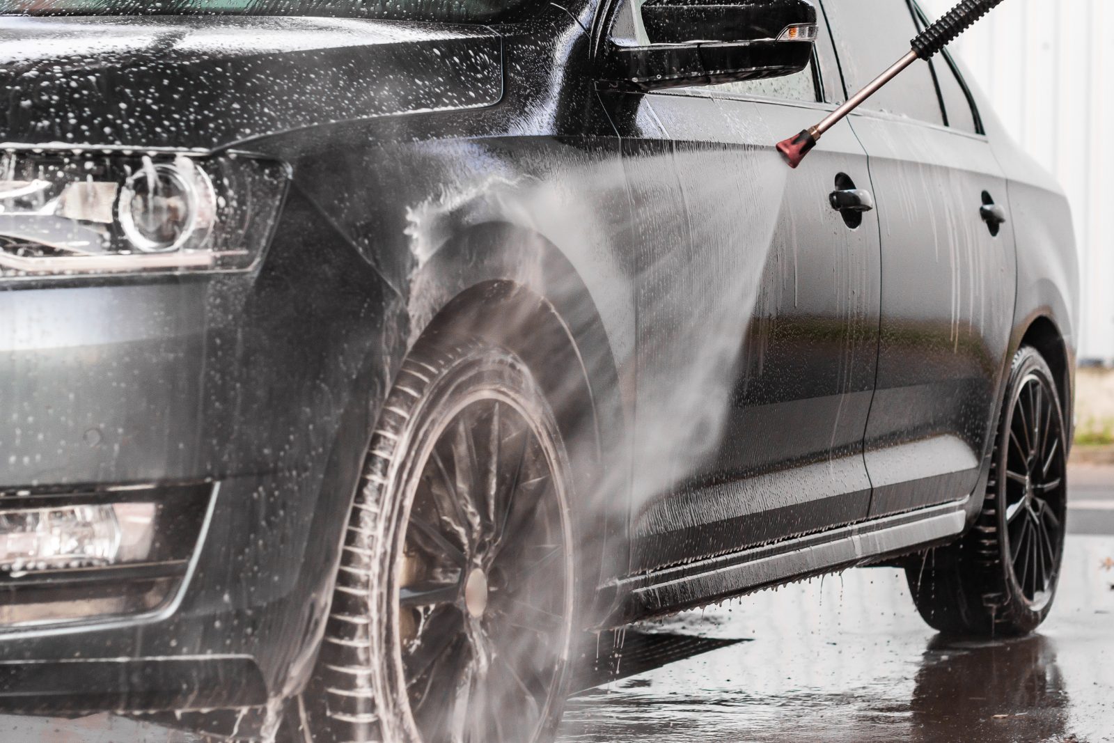 High-pressure water spray cleaning the side of a silver car at a car wash