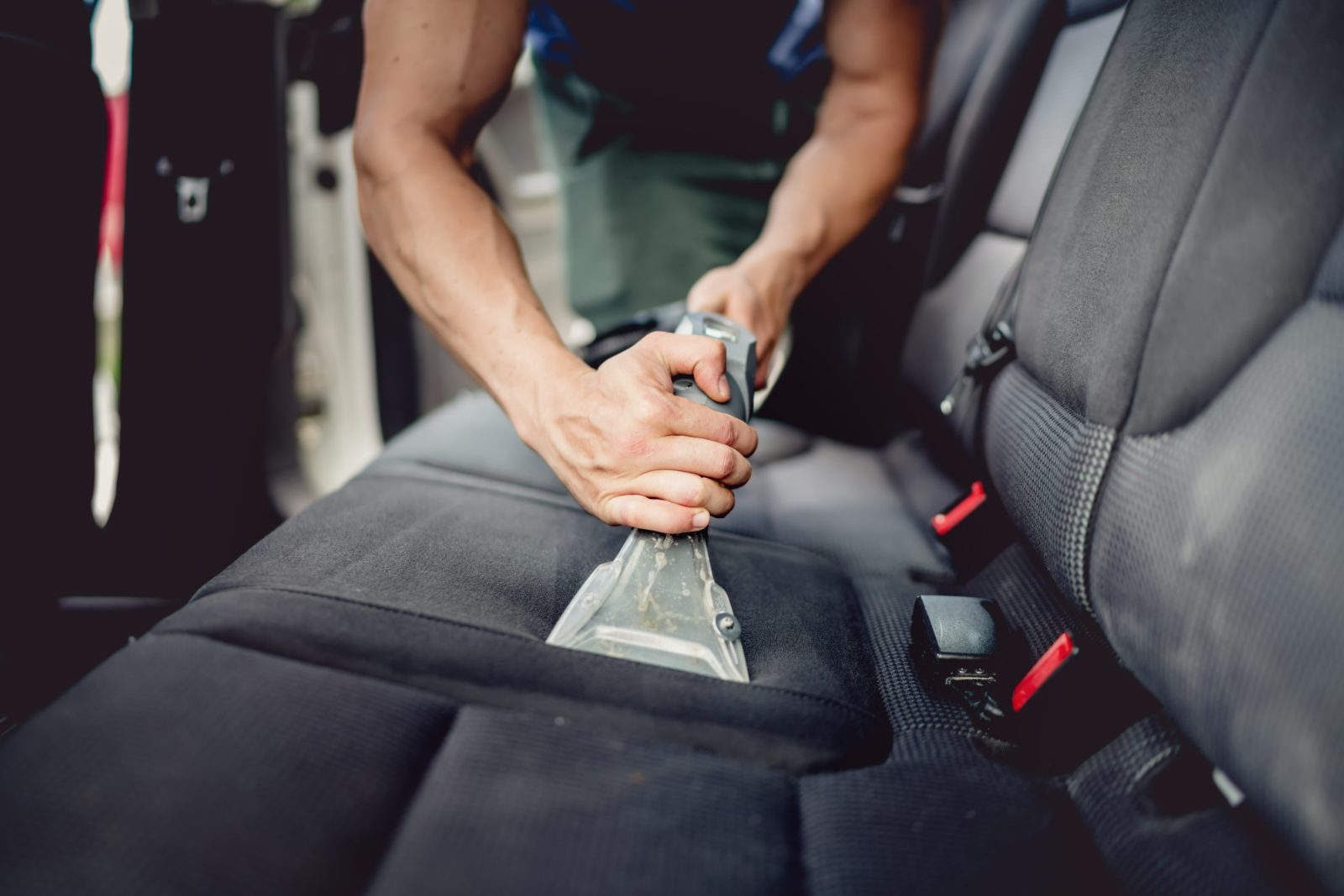 Person using handheld vacuum cleaner on car seat upholstery
