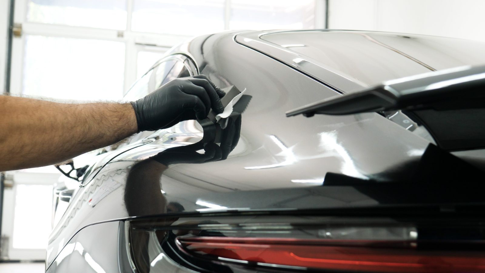 Professional detailing technician applying protective coating to silver car hood with microfiber cloth